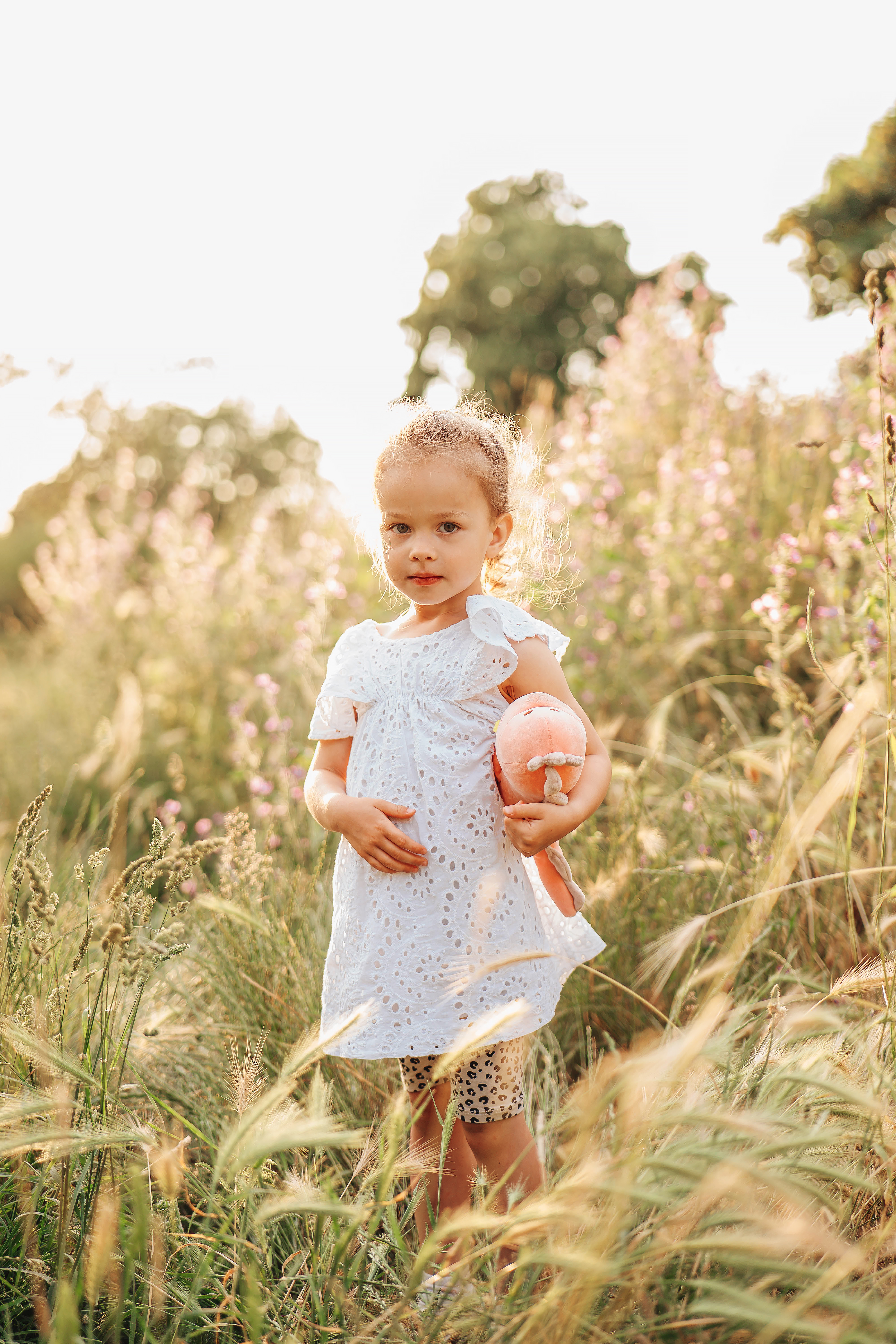 Small girl in high grass with a toy, sunset